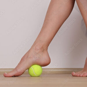 Woman Rolling tennis ball under arch of foot for plantar fascia pain