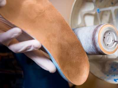 Man adjusting foot orthotic with grinding wheel | FootWebStar Pedorthist adjusting foot orthotic with grinding wheel